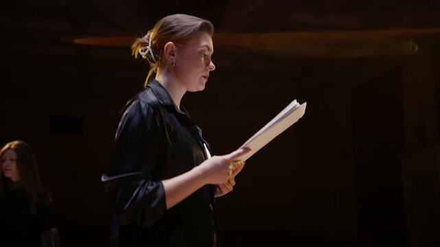 Focused theater rehearsal with two actors reading scripts on a dimly lit stage, practicing dramatic dialogue and performance under warm spotlight illumination