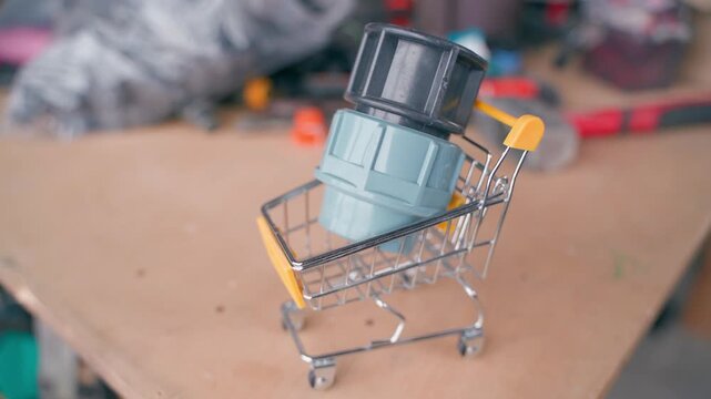 Hand placing plumbing pipe fitting into miniature shopping cart on workbench