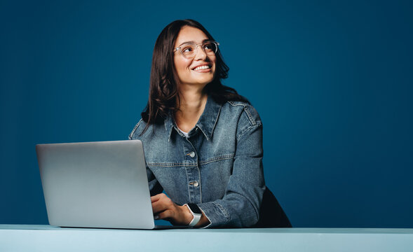 Woman working on laptop in studio with blue background and glasses