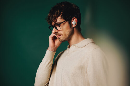 Young pensive man in glasses adjusting earbuds in studio portrait