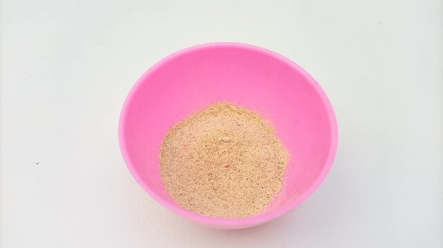 Traditional Ayurvedic Ubtan Powder Mixing Process in Pink Plastic Bowl with Mixing Spoon Isolated on White Background