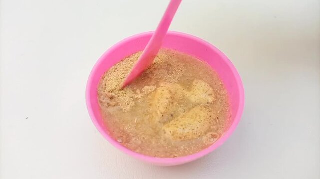 Traditional Ayurvedic Ubtan Powder Mixing Process in Pink Plastic Bowl with Mixing Spoon Isolated on White Background