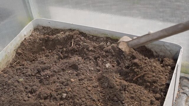 Top view of loosening soil with hoe in greenhouse garden bed in slow motion for planting preparation