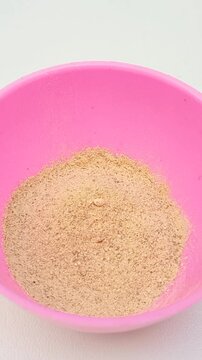 Traditional Ayurvedic Ubtan Powder Mixing Process in Pink Plastic Bowl with Mixing Spoon Isolated on White Background, vertical clip