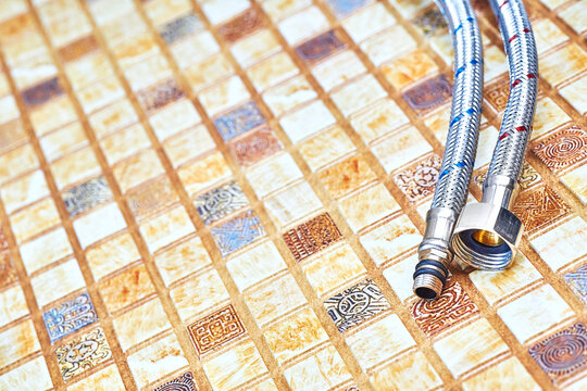 Plumbing. Flexible metal stainless steel faucet hoses on light brown pvc panel