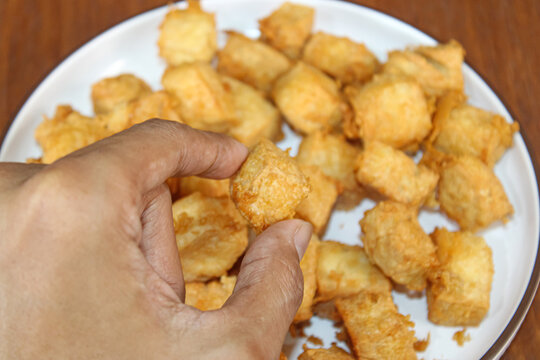 Hand picking a crispy golden fried tofu cube from plate
