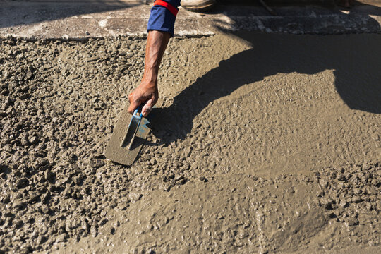 Construction worker's hand using a trowel to smooth fresh gravel mixed cement on a road surface
