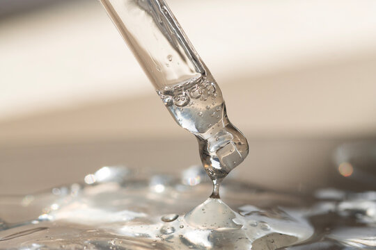 Serum in a pipette with a drop of liquid texture on a beige background with bright sunlight.