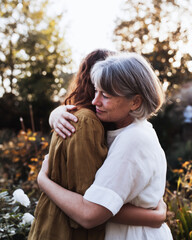 Naklejka premium Mother and adult daughter hugging warmly in sunlit garden