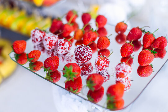 Fresh strawberries and coconut-covered fruit skewers arranged on a mirrored serving tray for dessert display