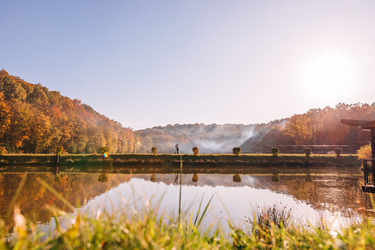 Romantic couple standing by a reflective lake in autumn light with misty trees and golden sunset