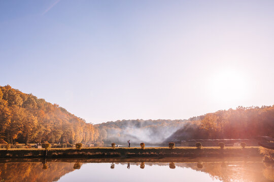 Couple walking by a misty lake at sunrise with autumn trees and golden reflections