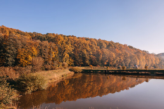 Couple walking along a lakeside path with autumn forest and golden reflections on calm water
