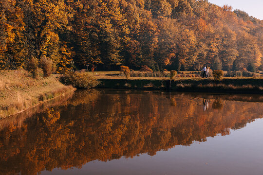 Couple walking by a lake with golden autumn trees and reflections on a calm pond