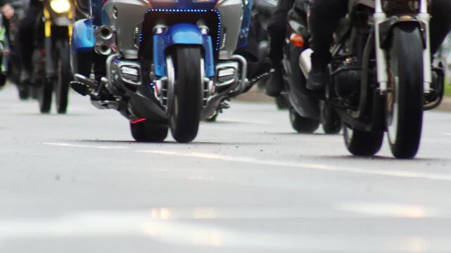Dynamic scene multiple motorcycles driving asphalt road. Close-up view front wheels, engines, lower parts. Reflections on road emphasize movement. Riders participate in group event, conveying freedom.