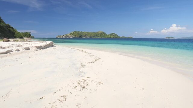 Pristine white sand beach and crystal-clear turquoise waters in Riung 17 Islands Marine Park, Flores, Indonesia, with small tropical islands on the horizon under a bright blue sky