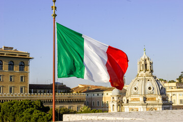 The Italian flag waves in front of historic buildings and a dome in Rome, Italy. © Nick