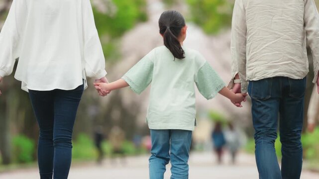 手を繋いで公園を歩く三人家族