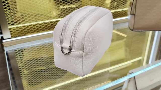 Detailed view of small rectangular white textured travel pouch, featuring two separate compartments secured by silver zippers and metallic ring for attachment, presented in bright retail display