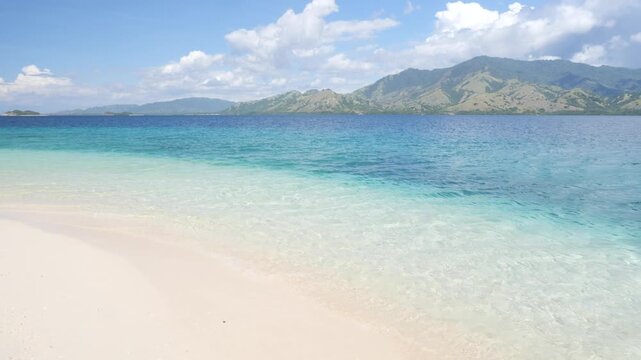 Pristine white sand beach and crystal-clear turquoise waters in Riung 17 Islands Marine Park, Flores, Indonesia, with small tropical islands on the horizon under a bright blue sky