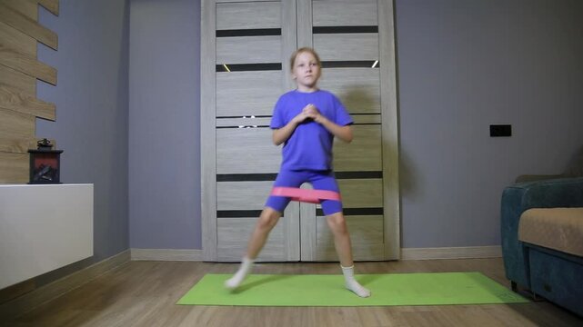 Caucasian preteen girl engages in physical activity, exercising with resistance band around thighs, home workout session, focus on strength and discipline, kid staying active indoors on green mat
