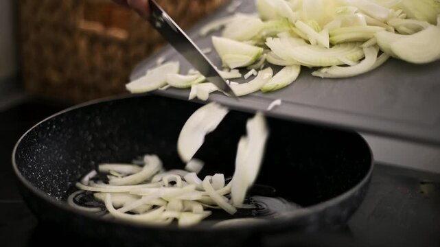 Man Tosses Chopped Onion From A Cutting Board Into A Sizzling Hot Frying Pan On The Stove