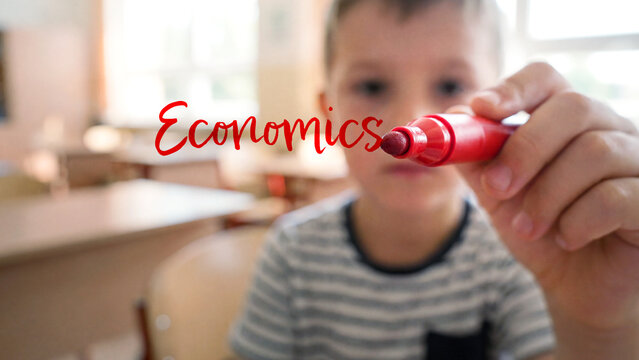 Child with red marker writing economics in school classroom, education learning in elementary setting, young student creativity knowledge concept