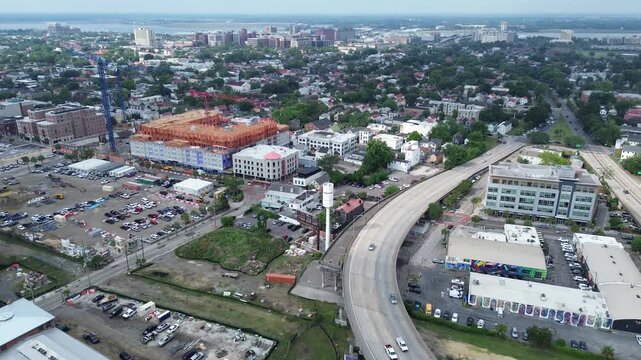 Elevated interchange view sweeps over Meeting St, Morrison Dr, framing NoMo blocks beside Ravenel Bridge approach. Mixed roofing, dense tree pockets, varied textures extend across Charleston, SC