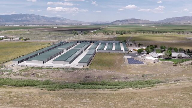 Aerial drone perspective flying backwards from a large self-storage unit facility located in a rural valley, with distant mountains under a partly cloudy sky in Minden, Nevada