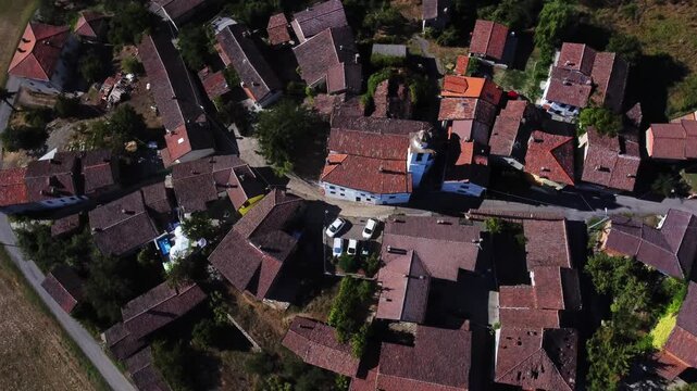 Vertical aerial drone shot capturing terracotta rooftops, narrow streets and the central church of a traditional Italian countryside village.
