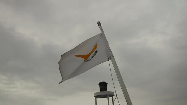 Cyprus national flag waves on boat mast with navigation light below under cloudy grey sky