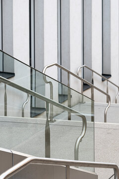 Black and white photograph shows glass railings and metal handrails across concrete stairs, with vertical facade lines shaping urban architecture