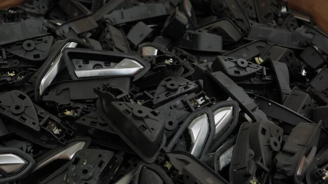 Large pile of black and chrome automotive interior door handle components sorted for plastic recycling