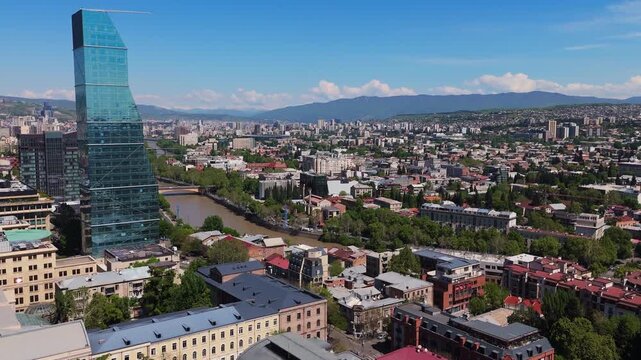 Aerial zoom out of the Biltmore Hotel skyscraper in Tbilisi, Georgia, capturing a close-up of its glass facade and modern architectural design against the city skyline