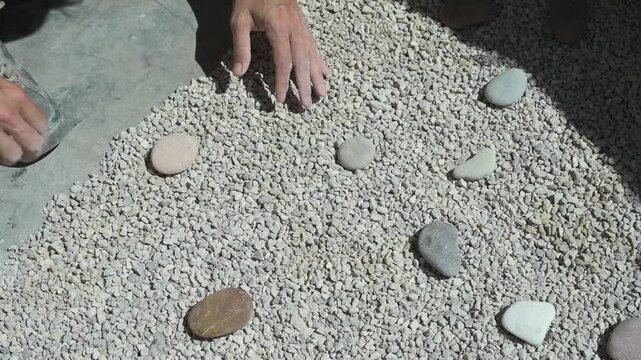 Male hands arranging smooth pebbles on a gravel bed in a japanese style rock garden
