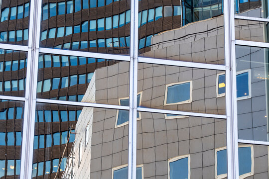 Glass facade holds reflections of another building across office windows, where urban architecture, grid lines and blue panels create layered depth