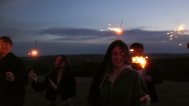 Happy group of multiethnic teenagers running with bright sparklers at night.