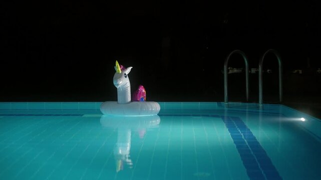 Bright unicorn float rests in an empty swimming pool during nighttime
