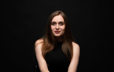 Naklejka premium Young woman with long brown hair smiling at camera, sitting on a chair against a black background