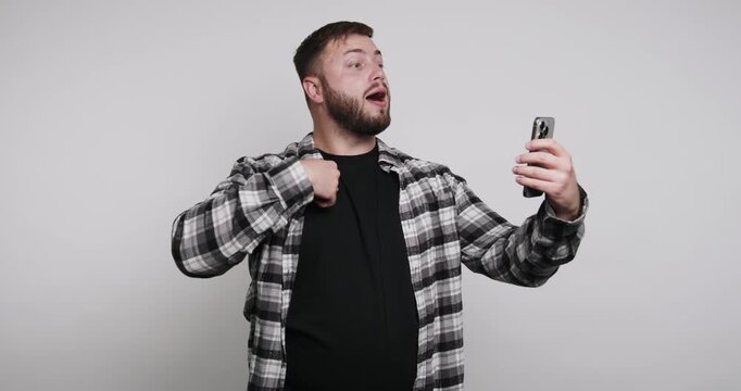 Man talks to camera while holding phone in simple indoor setting with light background