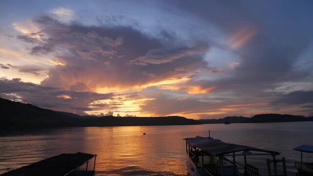 Vibrant sunset over Riung Bay and the 17 Islands Marine National Park, Flores, Indonesia, with traditional boats on calm water beneath dramatic orange, gold, and purple clouds