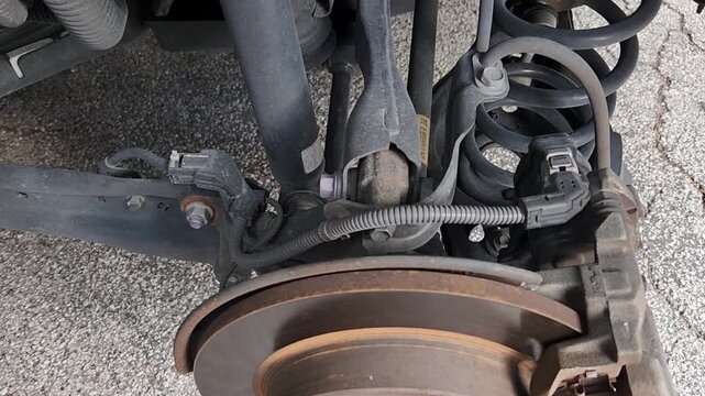 Video footage showing exposed brake rotor, brake caliper, suspension spring, shock absorber, and wheel hub after wheel removal during automotive maintenance. Detailed inspection of vehicle braking and