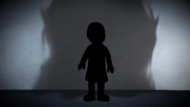 Static shot of silhouette child figure as shadow grows and transforms into looming shape on textured wall inside dark room
