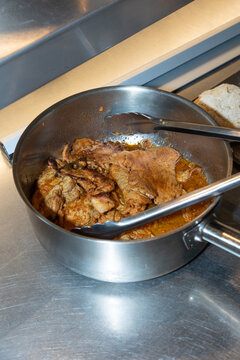 Traditional Portuguese bifanas cooking in a metal pan with flavorful sauce. Close-up of marinated pork steaks prepared in a professional kitchen, showcasing authentic Portuguese cuisine and comfort