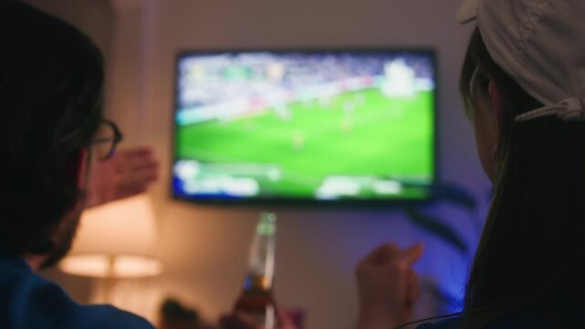 Friends at home watching a live football match, cheering and enjoying drinks, spending an exciting evening together during the World Cup. High quality 4k footage