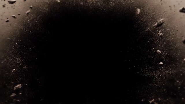 Slow motion closeup of debris and rock fragments exploding and scattering against black background in studio darkened interior