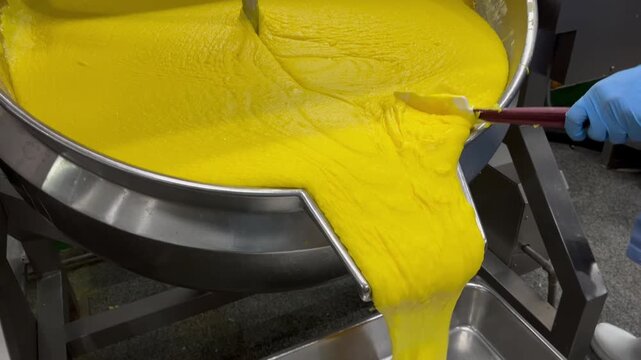 Prepared food filling being transferred from an industrial mixing kettle into containers for weighing and batch control. Food manufacturing process supporting product consistency, quality assurance, a