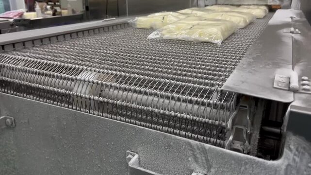 Packaged food products moving on a conveyor system into a spiral freezer during food manufacturing operations. Freezing process supporting product preservation, quality control, and large-scale frozen