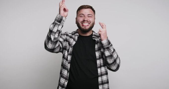 Man hopes for good luck while wearing a checkered shirt in a plain room during a happy moment