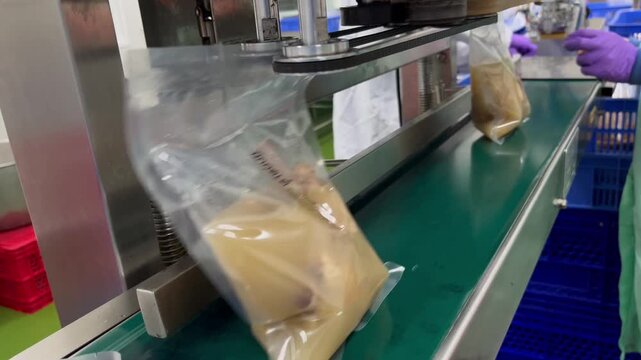 Food packages being sealed on an automated production line in a food manufacturing facility. Packaging process supporting product protection, quality control, and efficient food distribution.